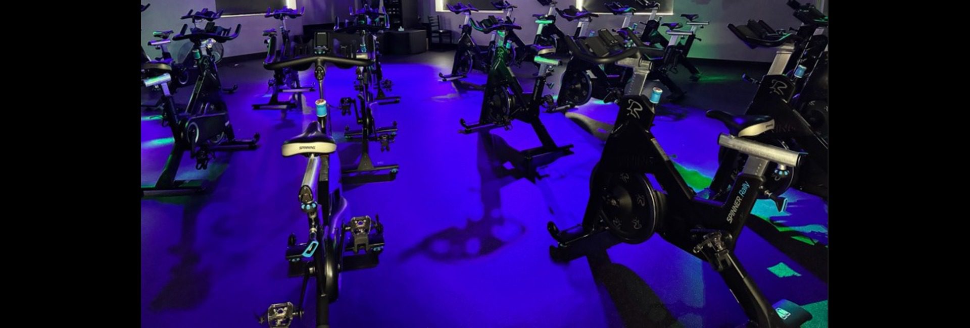 Princeton Club Fitchburg indoor cycling studio with rows of spin bikes and purple ambient lighting — renovated 2025 group fitness space