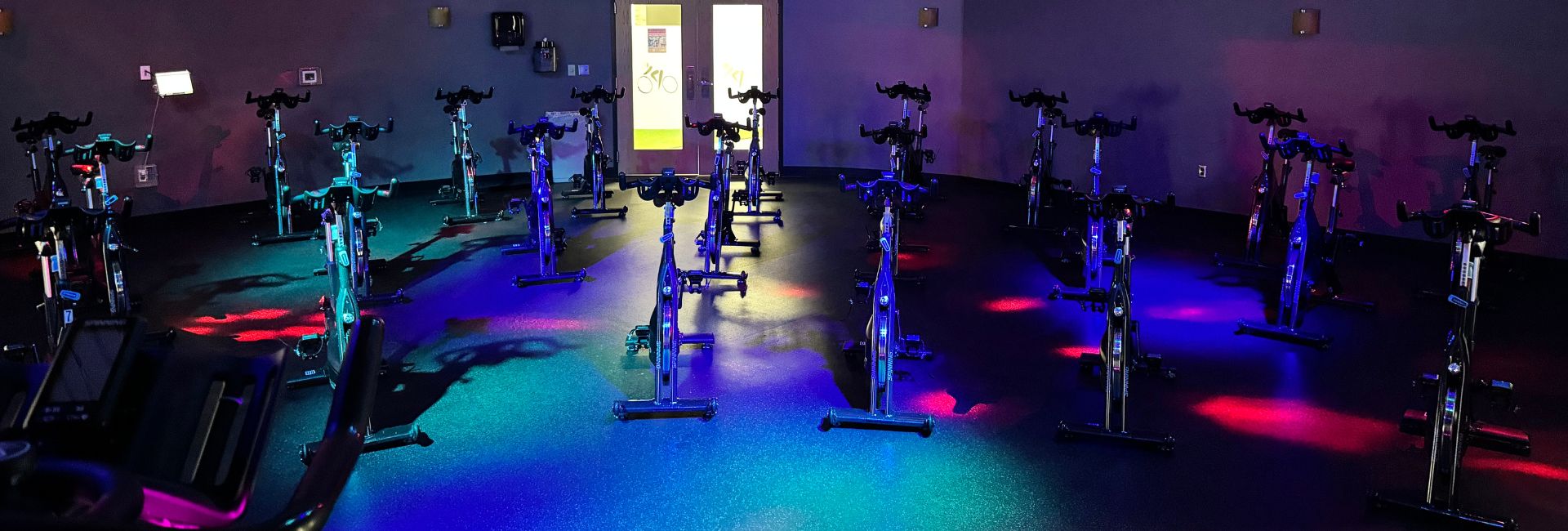 Indoor cycling studio at Princeton Club Fitchburg with stationary bikes under blue lighting, open 24 hours 7 days a week.